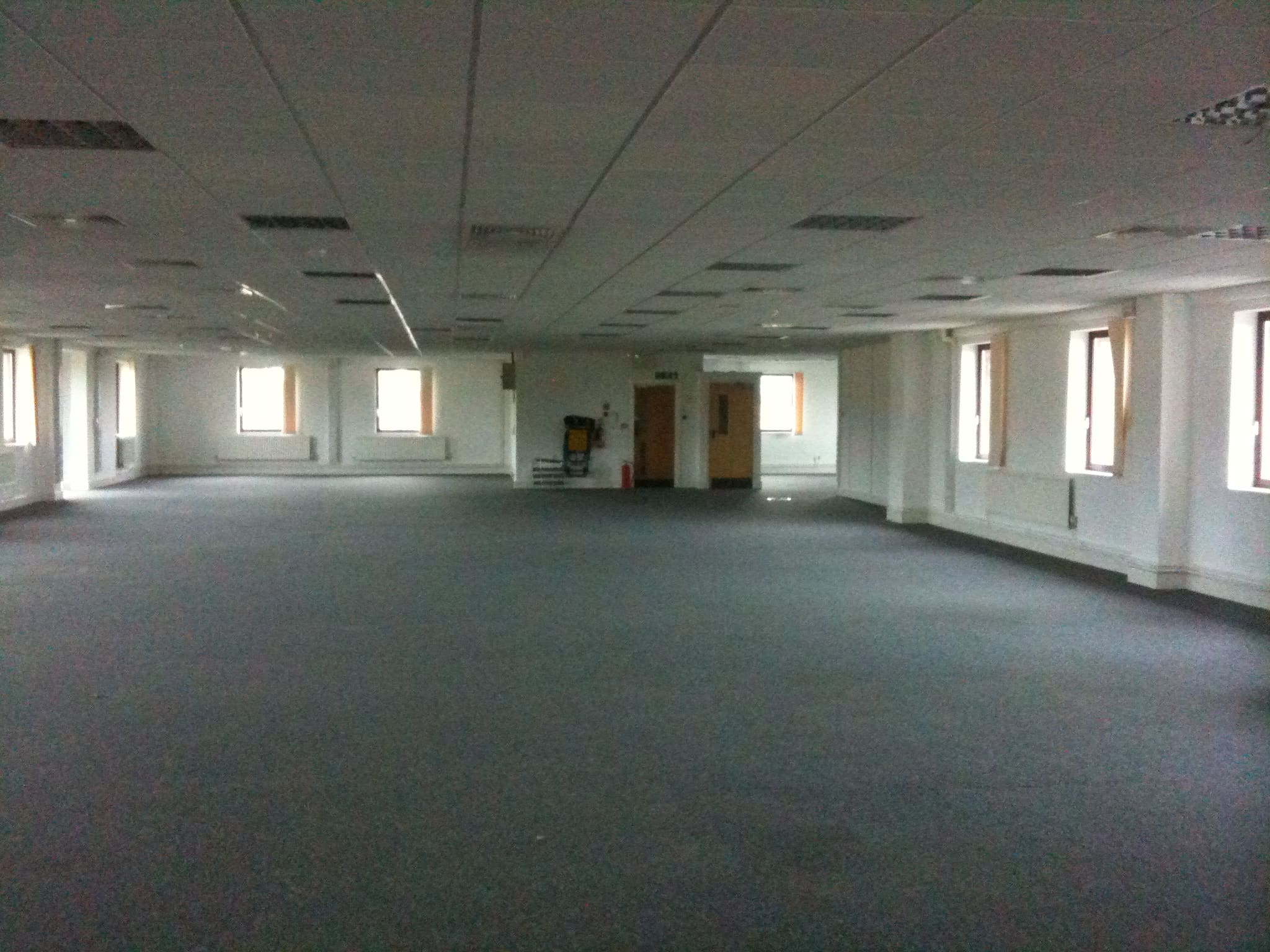 An empty office space with grey carpet and fluorescent lighting, an example of the liminal-space aesthetic associated with the Backrooms