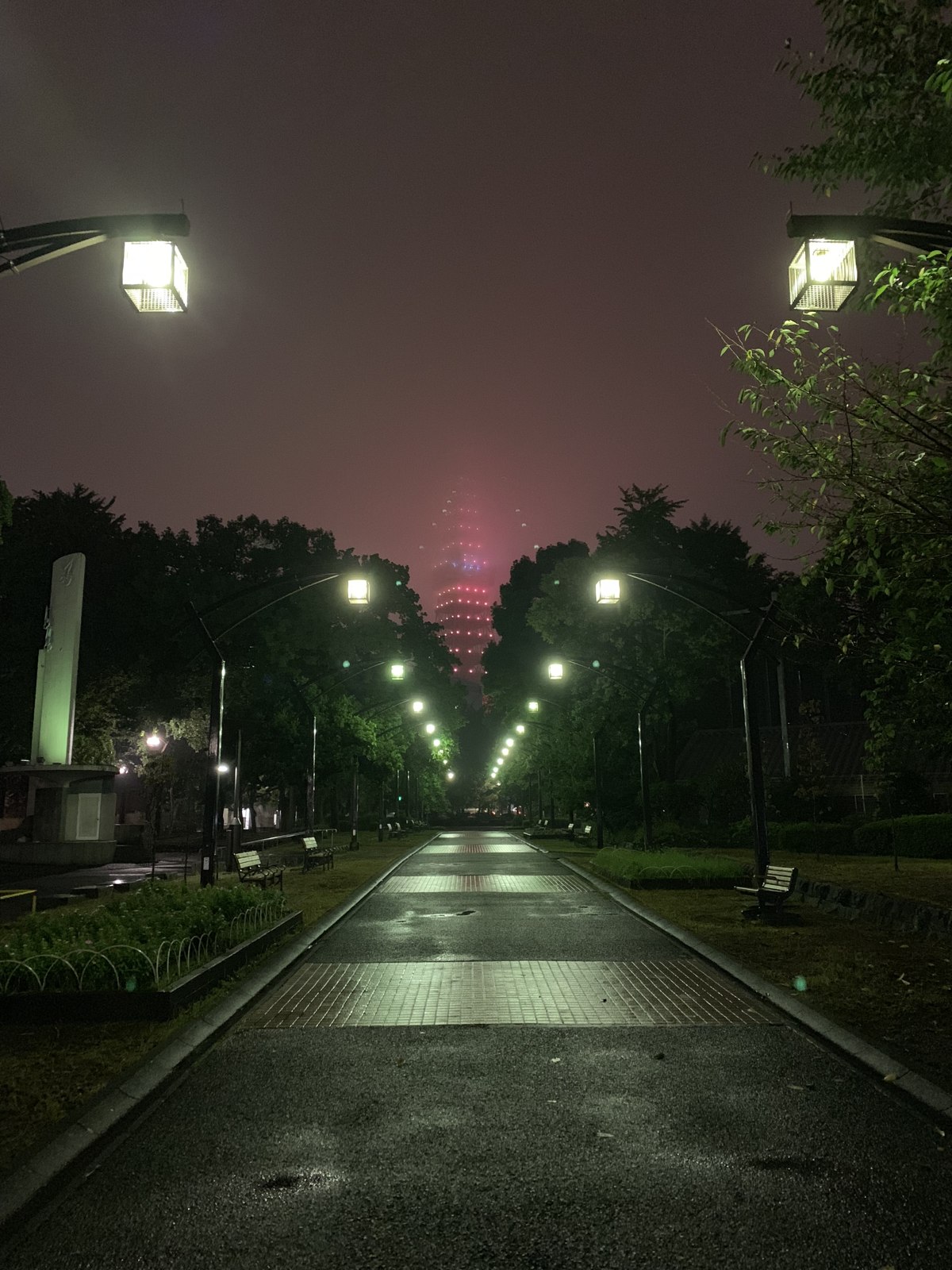The real Tokyo Tower at night in rain and mist, viewed from Shiba Park in 2018; setting context, not the fictional Elysium Tower or a game screenshot