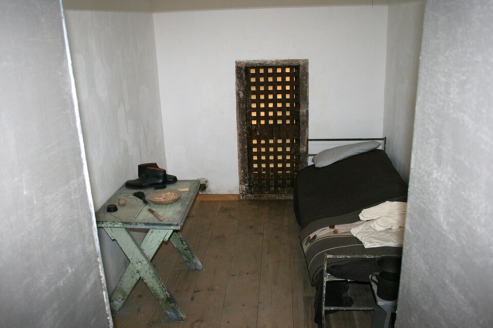 Restored interior of an Eastern State Penitentiary cell, showing a bed, table and small barred skylight