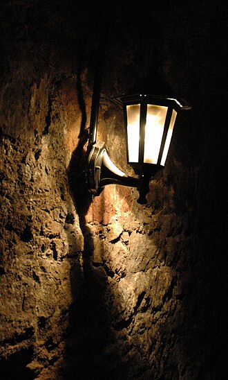 A lantern hanging on a rough stone wall in a narrow passage within the Edinburgh vaults