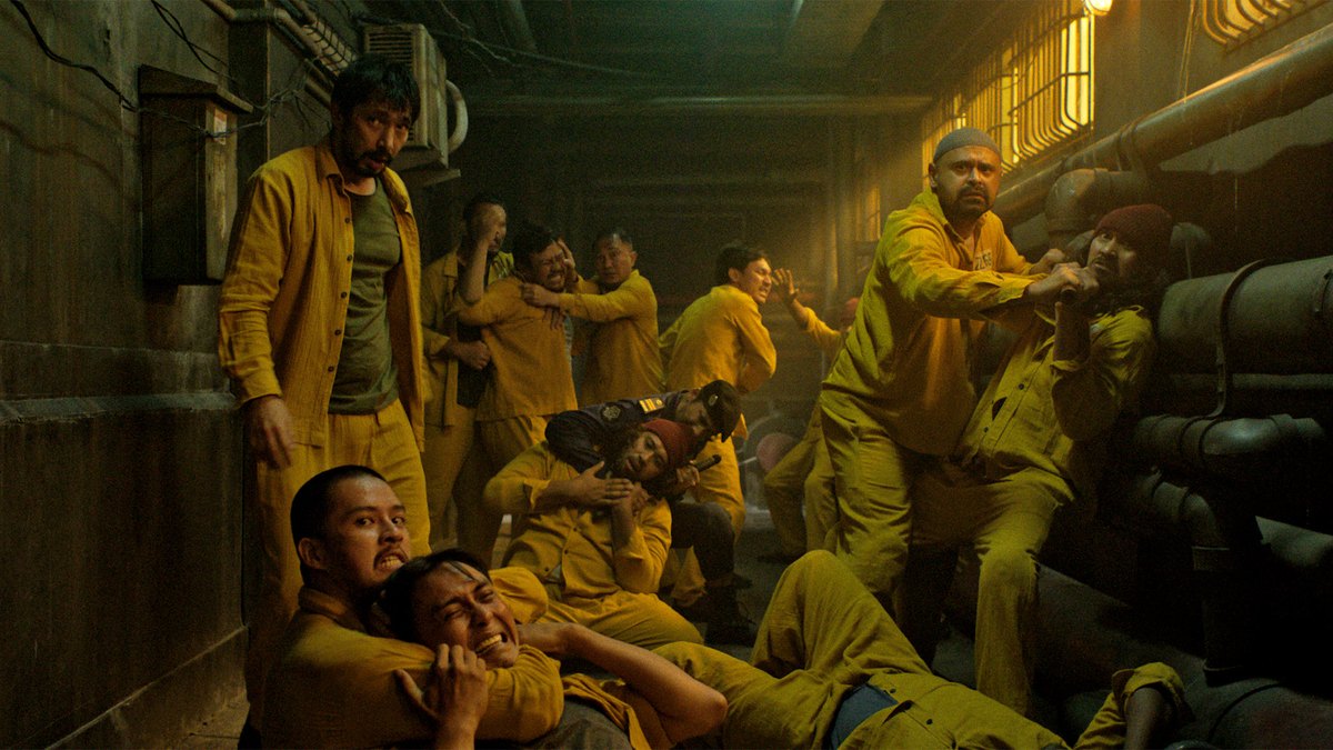 Prisoners in yellow uniforms fight in a dim corridor in Joko Anwar’s Ghost in the Cell