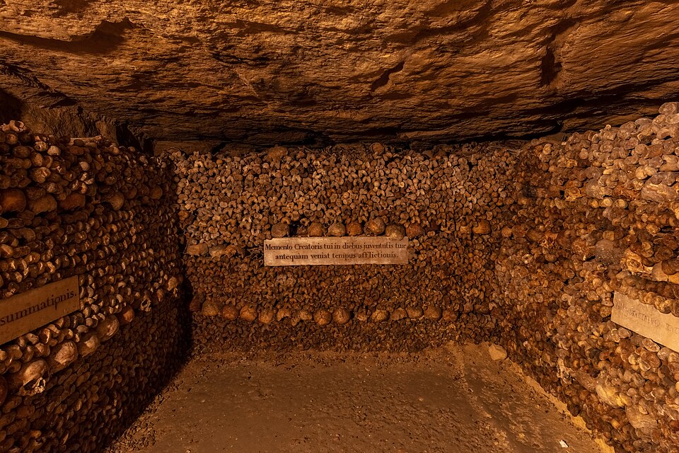 A gallery of the Paris municipal ossuary, with walls of skulls and long bones arranged around a stone inscription